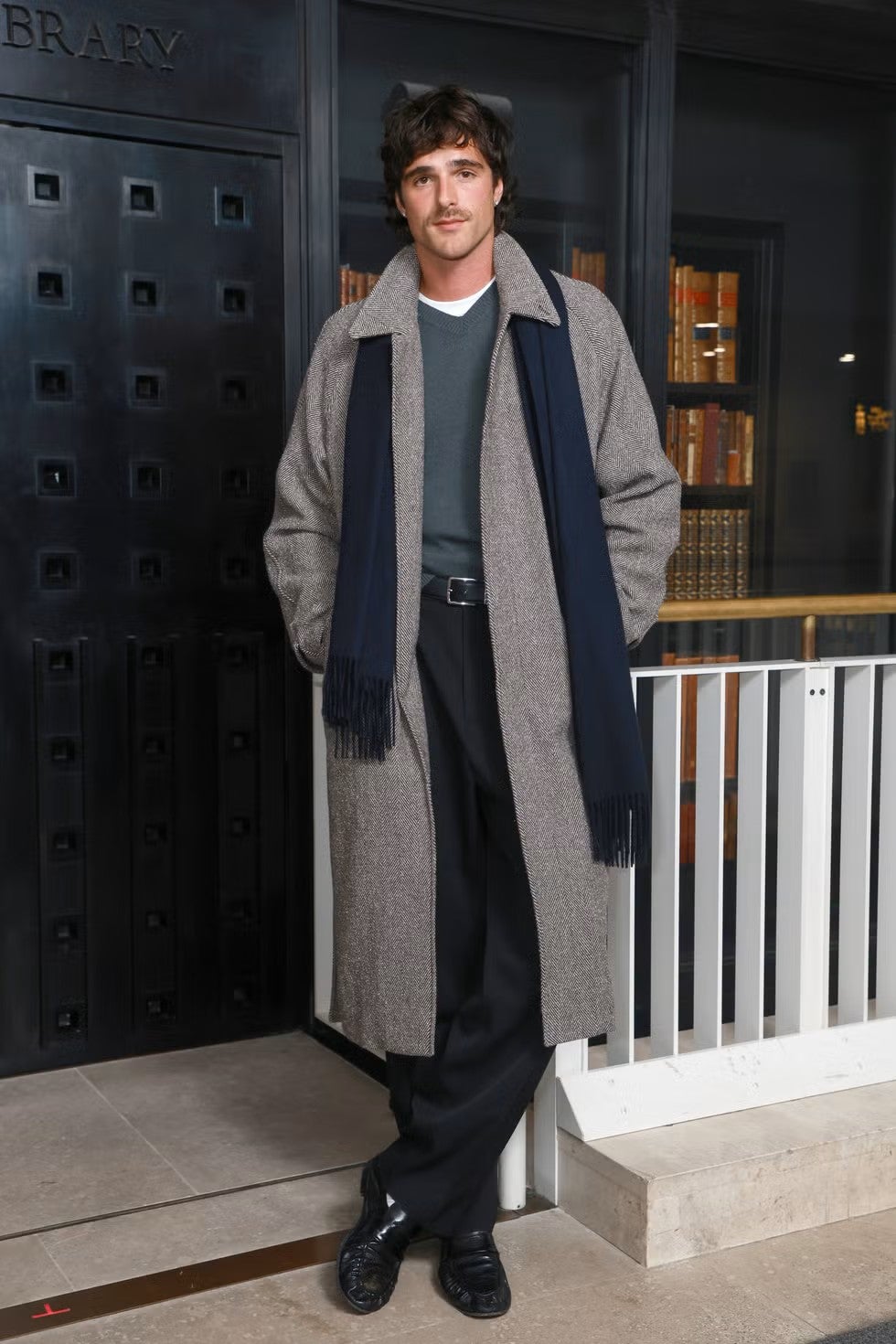Jacob Elordi combina un abrigo de espiga con una bufanda azul marino en un look donde las prendas exteriores cobran especial protagonismo | Getty Images