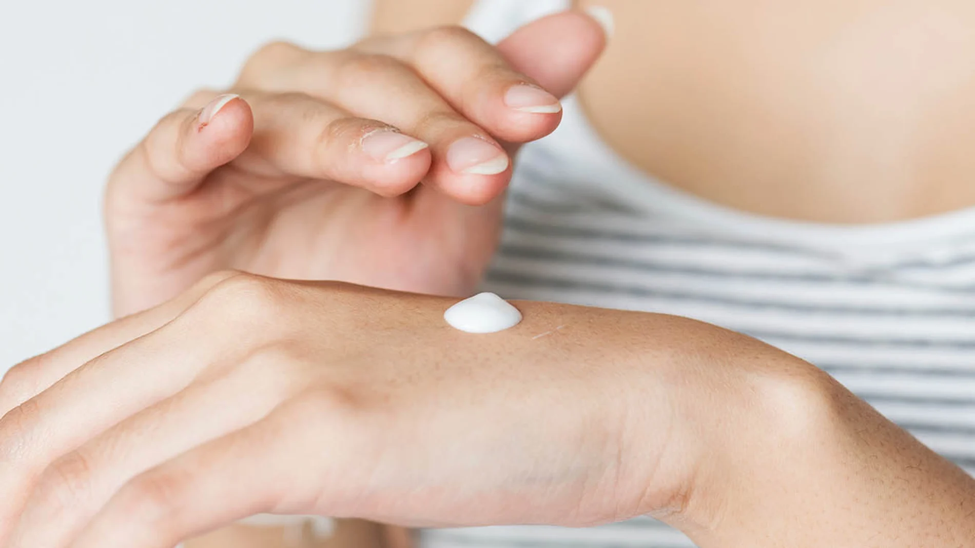 mujer echando crema en sus manos