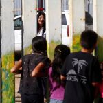 Una mujer habla, desde el lado de EEUU, con un grupo de niños mexicanos, separados por la vaya fronteriza que separa México de Estados Unidos