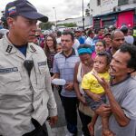 Un hombre con un niño en brazos grita consignas contra un policía en el barrio de Catia, a las afueras de Caracas