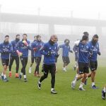 Zidane dando ánimos y la plantilla entrenándose ayer en Valdebebas, entre la niebla de Madrid
