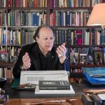 El novelista sentado en su estudio, delante de su biblioteca, en el escritorio donde suele escribir sus libros