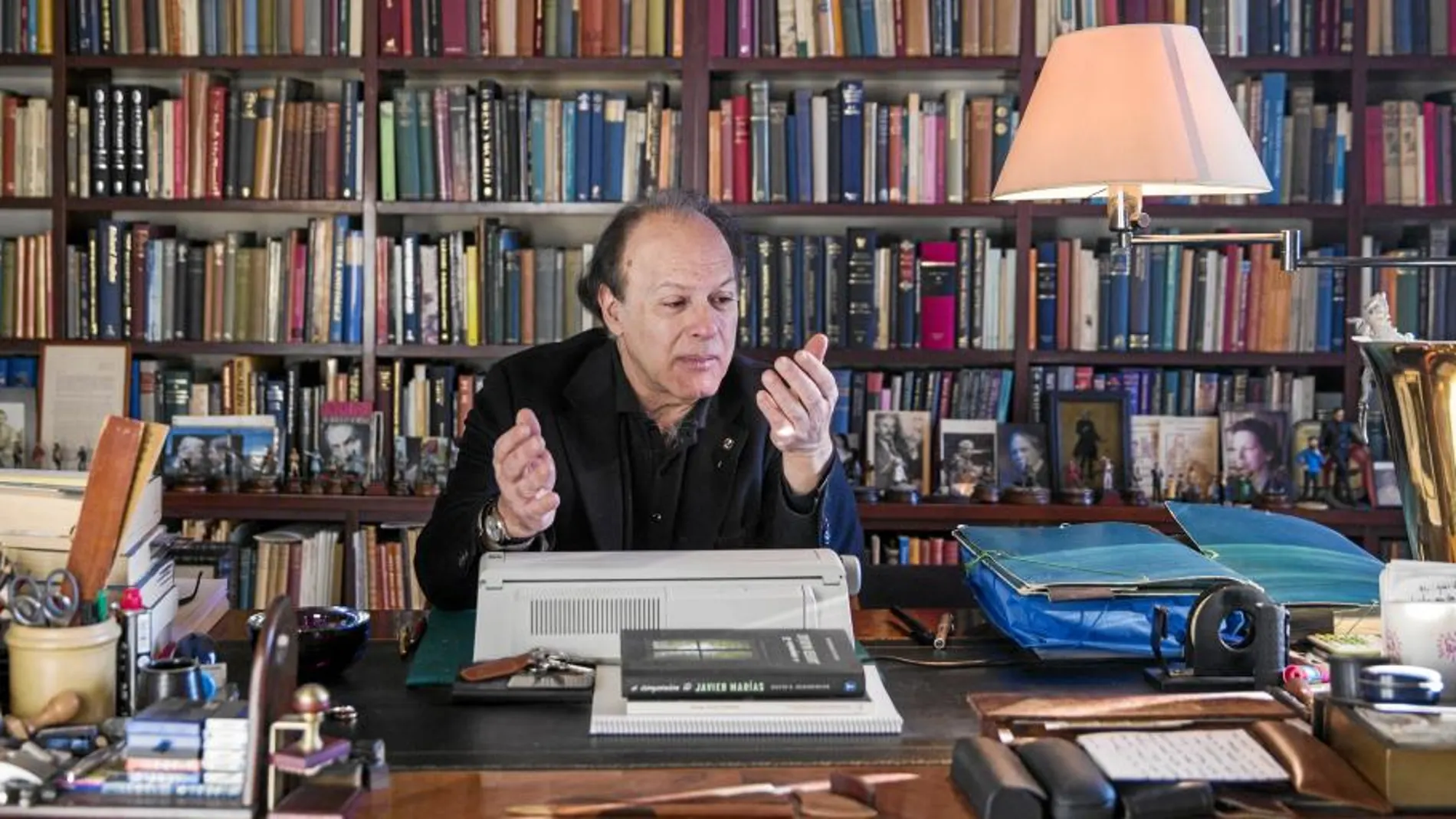 El novelista sentado en su estudio, delante de su biblioteca, en el escritorio donde suele escribir sus libros