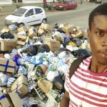 Un joven posa delante de un montón de basura acumulada en una calle de Luanda