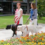 Dos usuarias pasean junto a sus perros guía a las puertas de la exposición en el parque de El Retiro