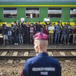 Un policía vigila mientras refugiados piden poder continuar su viaje rumbo a Europa Occidental.