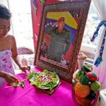 Una mujer venezolana ultima prepara la comida con una imagen de Hugo Chávez presidiendo el salón de su casa en Caracas