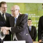 El jefe del Ejecutivo, Mariano Rajoy (i), abraza al primer presidente electo de la Xunta de Galicia, Xerardo Fernández Albor (c), antes de imponerle la Medalla de Oro al Mérito en el Trabajo, junto al presidente de la Xunta, Alberto Núñez Feijóo