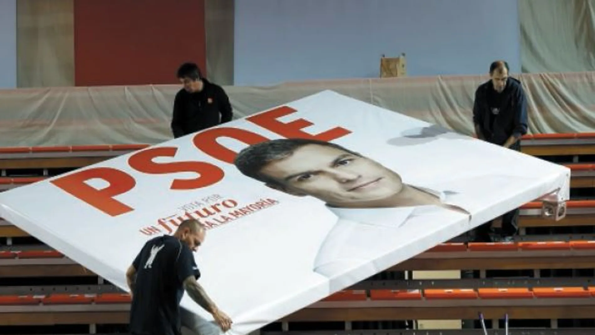 Tres operarios retiran un cartel electoral de Sánchez, tras un mitin