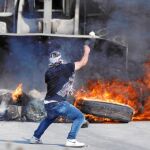 Un joven palestino arroja piedras contra una excavadora israelí en la aldea de Kobar, de donde salió el joven que mató el viernes a tres colonos israelíes