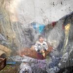 Un niño se encuentra sentado detrás de unos plásticos que cubren las tiendas de campaña de un campamento improvisado en Idomeni, Grecia