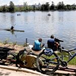 Varias personas junto a sus bicicletas descansan hoy junto al lago de la Casa de Campo de Madrid aprovechando las agradables temperaturas registradas en la capital.