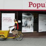 Un repartidor pasa ante una oficina del Banco Popular en el Paseo de Gracia esquina con la calle Aragón de Barcelona.