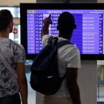 Unos pasajeros comprueban la anulación de un vuelo de Air France en un panel informativo.