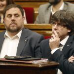 El presidente de la Generalitat, Carles Puigdemont (d), y su vicepresidente, Oriol Junqueras, en el Parlament de Cataluña donde se celebró un pleno monográfico sobre la situación de emergencia social, a petición del PSC y CSQEP, el pasado día 9