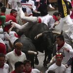 Dos astados de la ganadería de Miura, de Lora del Río (Sevilla), voltean a un mozo en el tramo final que precede al callejón de entrada a la Plaza de Toros durante el octavo y último encierro de los Sanfermines