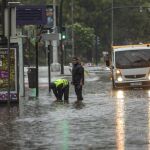 Dos operarios del ayuntamiento de Murcia intentan desatascar una boca de alcantarilla para desalojar el agua acumulada en la avenida Teniente Flomesta