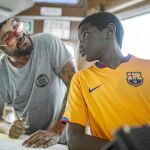 Un voluntario conversa en el Open Arms con un niño que lleva la camiseta del Barcelona / Ap
