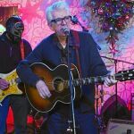 Nick Lowe, en el centro, delante de la enmascarada banda de surf rock Los Straitjackets