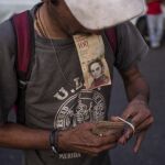 Un hombre organiza sus billetes de 100 bolívares mientras hace fila en las inmediaciones del Banco Central de Venezuela