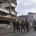 Fotografía facilitada por la Agencia Árabe Siria de Noticias (SANA) que muestra a varios hombres armados junto a los edificios del distrito de Al Sukari y Ansari de Alepo