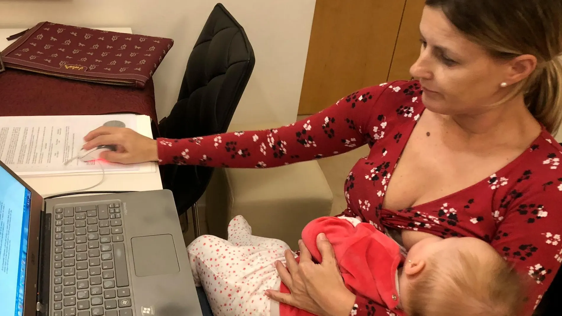 Una madre trabaja con su hijo en brazos
