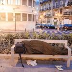 Una persona sin hogar descansa en un banco de la Gran Vía Ramón y Cajal de Valencia