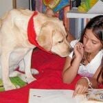 Una niña lee un cuento en voz alta ante la atenta mirada de uno de los dos labradores de READ España