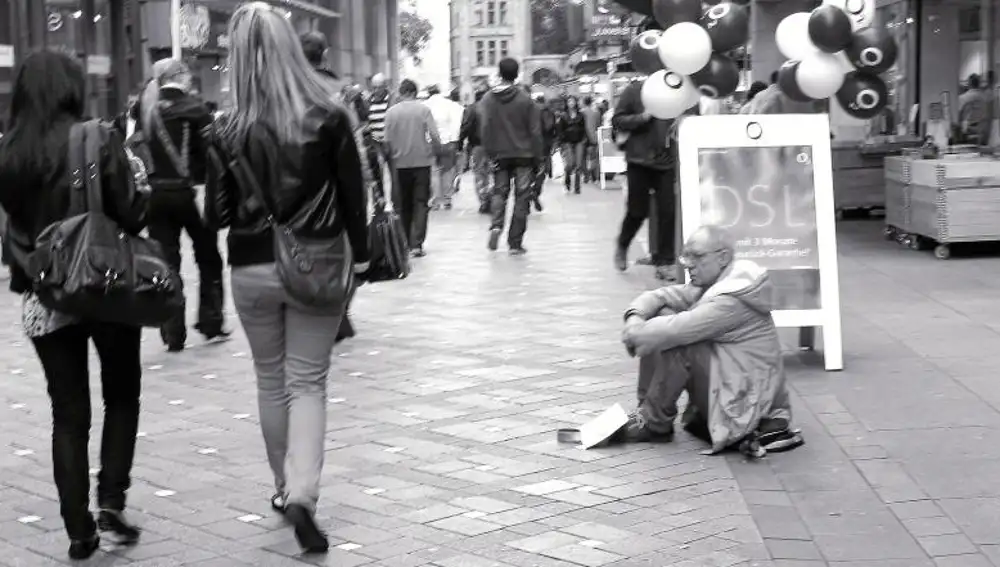 Un hombre pide limosna mientras varios ciudadanos pasean por el centro de una ciudad alemana