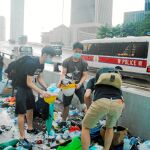 Varios jóvenes recogen cascos y paraguas de entre la basura generada tras las cargas policiales / Reuters