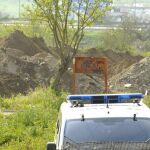 Una patrulla de Policía vigila la escombrera de Camas, con la máquina excavadora trabajando al fondo