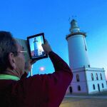 Un hombre aprovecha la caída del sol y la buena climatología para realizar una fotografía al faro del puerto de Málaga