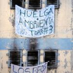 Un recluso saluda en las celdas cercanas al lugar donde murieron 81 presos entre carteles de protesta por la situación del presidio