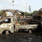 Un grupo de jóvenes curiosea junto a los restos de dos vehículos incendiados durante los incidentes para protestar contra los atentados en Karachi