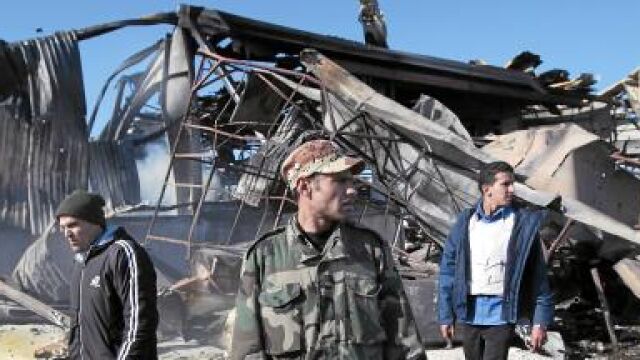 Soldados gadafistas pasan junto a un almacén destruido por los misiles aliados