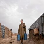 Un joven afgano porta unas garrafas en el campamento de refugiados