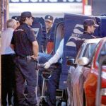 Varios policías observan cómo los servicios funerarios proceden al traslado de los cadáveres