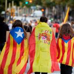 Tres jóvenes ataviados con banderas de España y esteladas se dirigen a la manifestación en la que miles de personas recorren las calles de Girona