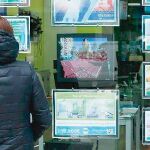 Ciudadanos observan un panel con distintas ofertas de vivienda en propiedad
