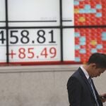 Un hombre mira su móvil junto a unos paneles con los indicadores de la bolsa en Tokio. (AP Photo/Koji Sasahara)