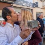 Los agraciados con un número del gordo de Navidad Yesica Garcia y Alexander Zambrano se besan monstrando el número premiado en su móvil hoy en la puerta del obrador donde lo compraron. La administración Virgen de La Salceda de Las Torres de Cotillas ha consignado cinco series del número 26.590, agraciado con el Gordo de Navidad, dotado con cuatro millones de euros por serie (400.000 euros por décimo). EFE/Marcial Guillén