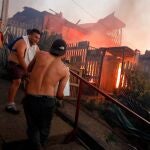 GRAF4255. VALPARAISO, 25/12/2019.- Varias personas intentan sofocar las llamas en sus viviendas que se han visto afectadas por un incendio forestal que alcanzó ayer martes un sector poblado de la ciudad costera de Valparaíso, mientras decenas de dotaciones de Bomberos y aeronaves tratan de controlar la situación desde tierra y aire. Desde las 15.00 hora local (18.00 GMT) dos focos diferentes de fuego se generaron de manera simultánea en los cerros de la ciudad de Valparaíso, a unos 100 kilómetros al este de Santiago, y avanzaron por los costados hasta juntarse y alcanzar la zona poblada periférica. EFE/Leandro Torchio