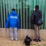 Un aficionado del Málaga C.F, junto a un reportero gráfico miran por unos agujeros de la valla que cierra y rodea el campo de fútbol de Ciudad de Málaga, donde el equipo malacitano ha entrenado hoy, a puerta cerrada, sin su técnico hasta ahora Víctor Sánchez del Amo, que ha sido suspendido "de sus funciones de forma inmediata" después de que se haya difundido un vídeo suyo de carácter íntimo por las redes sociales, hoy en la capital malagueña. EFE/Jorge Zapata