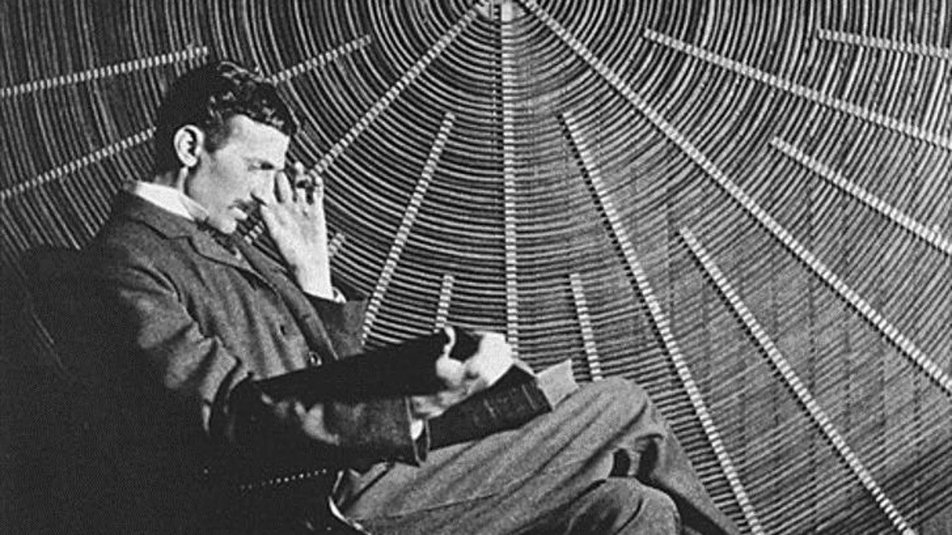 Nikola frente a una bobina de Tesla en su laboratorio de Nueva York, leyendo "Theoria Philosophiae Naturalis"