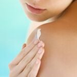 Extreme close up of a young woman applying lotion over her shoulder