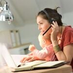 Una madre teletrabja con su bebé en brazos