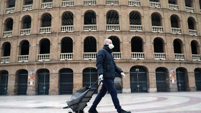 Una persona protejida con mascarilla y guantes pasa ante la plaza de Toros e valencia, hoy, sexto día desde que entró en vigor el Decreto de estado de alama.
