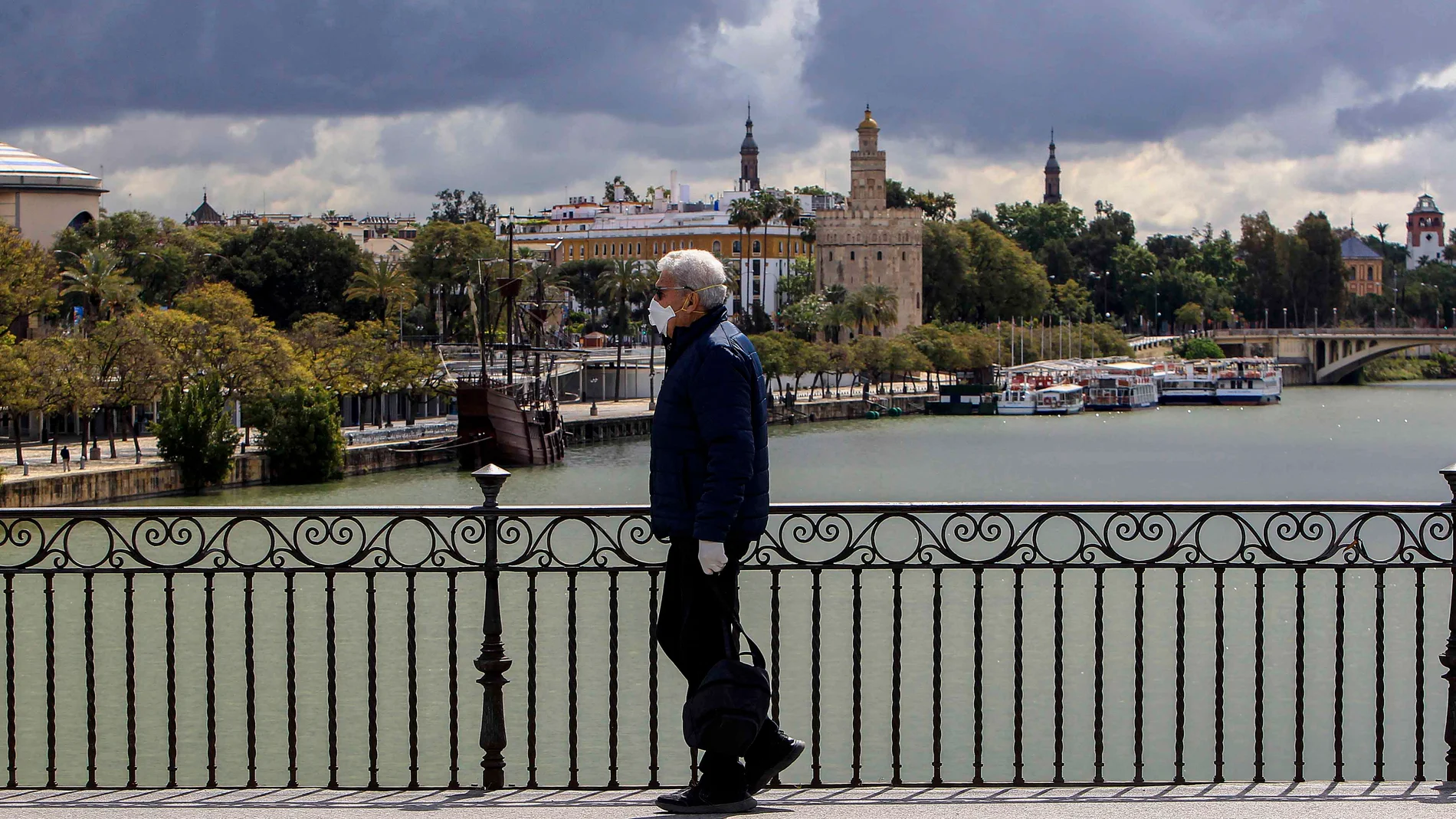Un hombre pasea por el Puente de Triana de Sevilla con una mascarilla y guantes