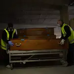 Dos trabajadores protegidos con mascarilla y guantes colocan un ataúd en el tanatorio de campaña de Collserola, situado en las dos plantas de parking del Tanatorio de Collserola, en abril de 2020