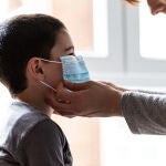 Una madre coloca a su hijo una mascarilla